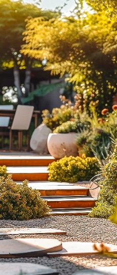 Jardin moderne : escalier de bois et terrasse paysagère Escalier en bois montant vers une terrasse ensoleillée, entouré de buissons. Pas japonais ronds sur gravier clair et poterie paysagère.